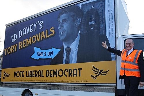 Photo of Lib Dem leader Ed Davey in front of poster van. Poster van reads "Ed Davey's Tory Removals" "Vote Liberal Democrat" A large arrow with the words "Time's up" points to an image or Rishi Sunak outside 10 Downing Street.